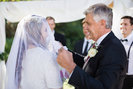 happy father removing veil of his daughter during wedding